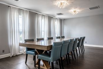 A long wooden table with blue chairs is in the middle of a room with a window.